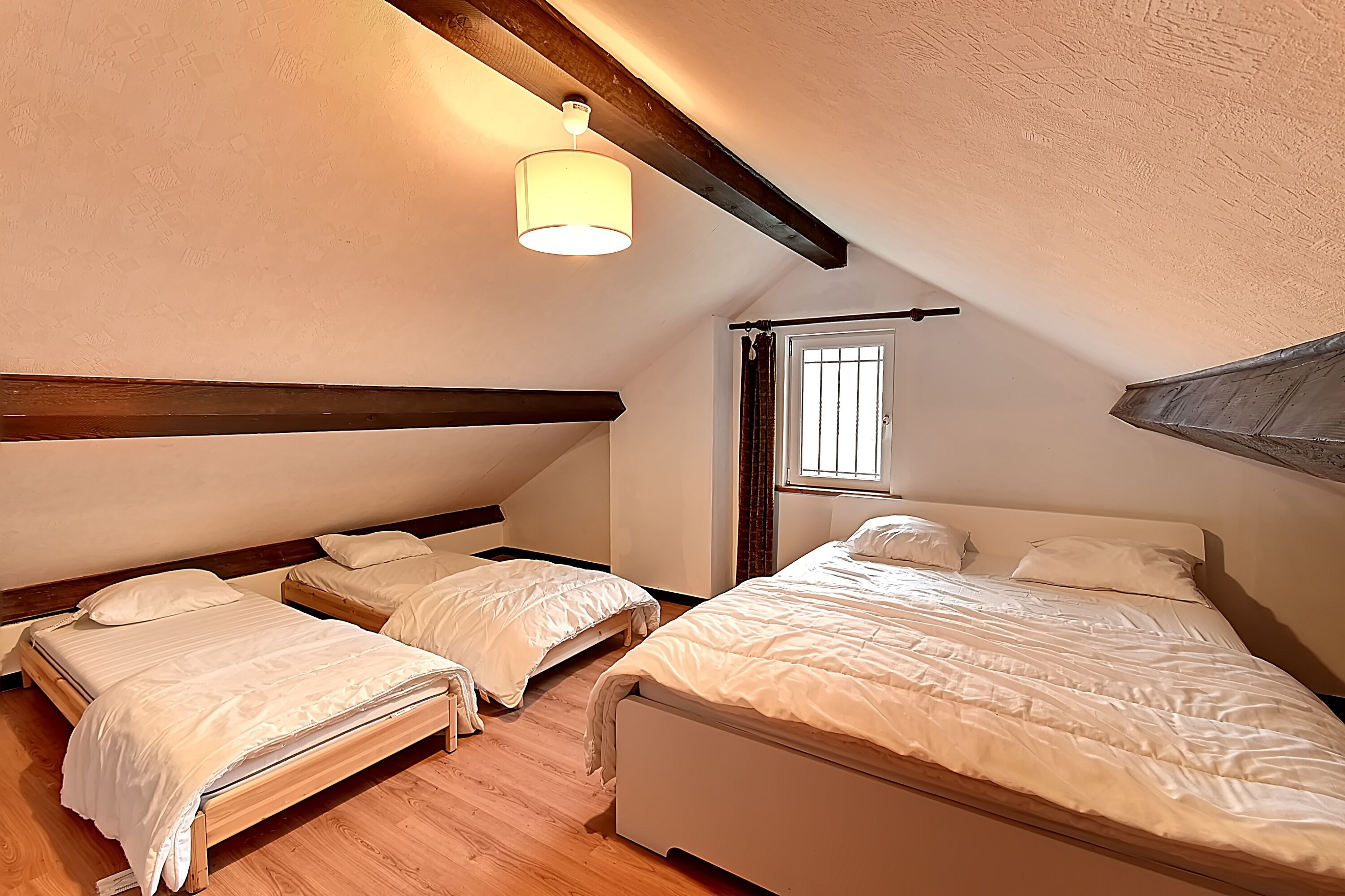 A bedroom with two single beds, a wooden ceiling, and a window with curtains.