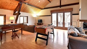 Un salon spacieux doté d’un parquet, d’un piano, d’un baby-foot, d’un canapé et d’une cheminée.