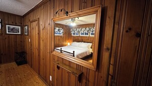 Une pièce aux murs lambrés, avec un lit placé au centre, juste en dessous d’un grand miroir.