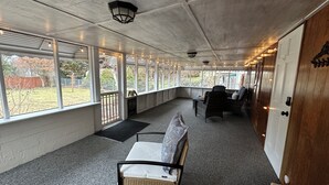 Un patio abrité, équipé d’un banc, de chaises et offrant une vue sur l’extérieur.