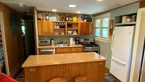 A compact kitchen with wooden cabinets, a central island with stools, a refrigerator, and a window providing natural light.