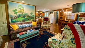 A cozy living room with a plaid sofa, a floral armchair, and a painting of a landscape.
