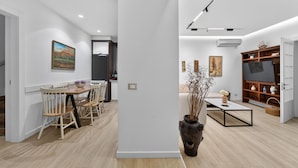 A modern living room with a dining area, wooden flooring, and a large flat-screen TV.