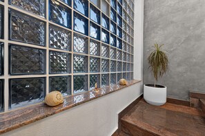 Una ventana con un diseño de vidrio texturizado, una planta en maceta y conchas decorativas en un repisa.