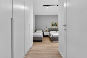 Un estrecho pasillo que conduce a un dormitorio con dos camas, una mesita de noche, una lámpara de pared y un cuadro.
