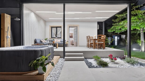 A modern outdoor living space with a hot tub, seating area, and a view of the garden.
