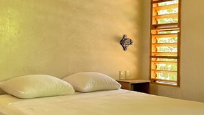 Un dormitorio con cama, ventilador de techo, lámpara de pared y ventana con persianas de madera.