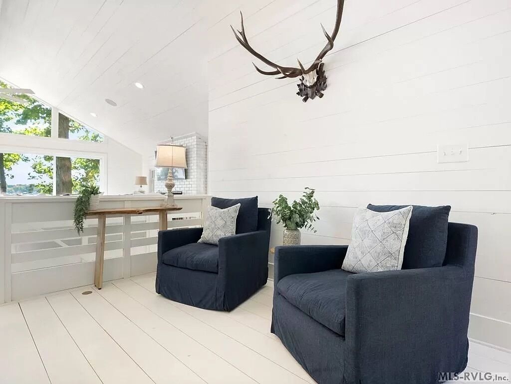 Een moderne woonkamer met twee donkerblauwe banken, een houten salontafel en een opgeplakt hertenhoofd aan de muur.