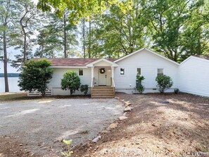 A single-story house with a front porch, a small front yard with a gravel path, and a lake in the background. - Newly renovated beauty on main lake with sunrise to sunset panoramic views! (Henrico)