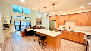 A modern kitchen with a large island, wooden cabinets, and a dining area with a view. - Slopeside Luxe-Upgrade Adventure (Conway)