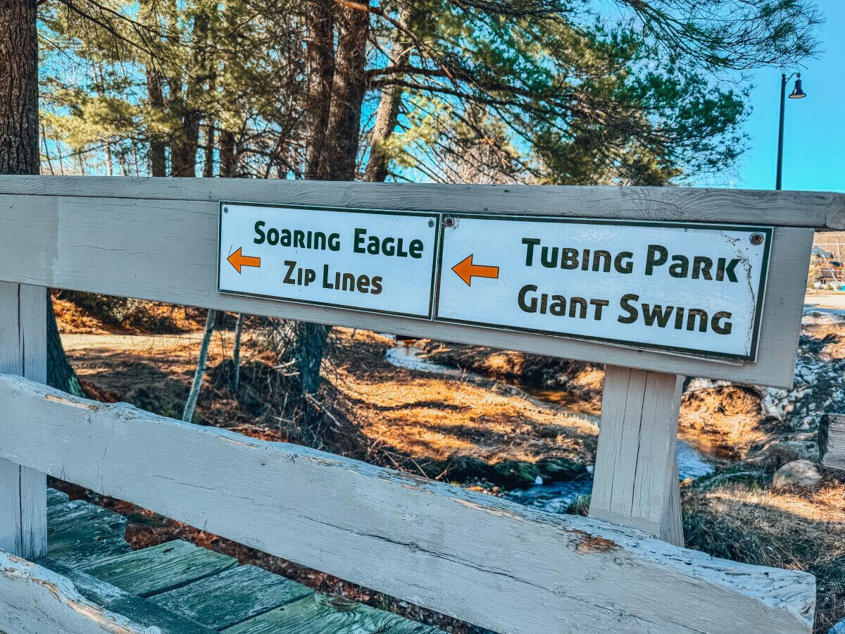 Un letrero de madera con flechas direccionales que indican 'Soaring Eagle Zip Lines' y 'Tubing Park Giant Swing'.