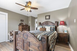 Une chambre à coucher avec un lit en bois, un ventilateur de plafond, une table de chevet, une chaise et une lampe.