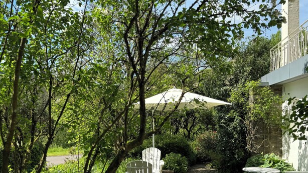 Um jardim com um caminho pavimentado, uma cadeira branca, uma mesa e uma fonte para pássaros.