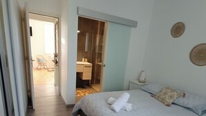 A bedroom with a bed, a bedside table, a hanging light, a wardrobe, and a bathroom visible through an open door. - Appartement T3 Refait à Neuf Calme et Centrale, Parking Privé, 5min de la Gare (Tours)