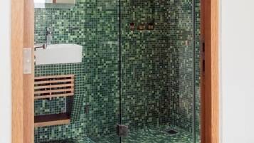 Un baño con baldosas verdes de mosaico, una cabina de ducha de vidrio y un lavamanos blanco.