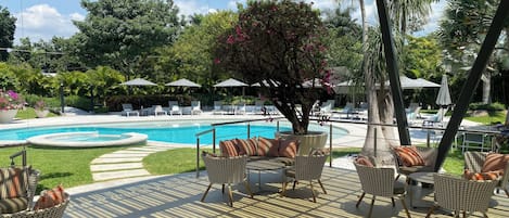 Un área junto a la piscina con sillones de descanso, sombrillas y una zona de estar techada.