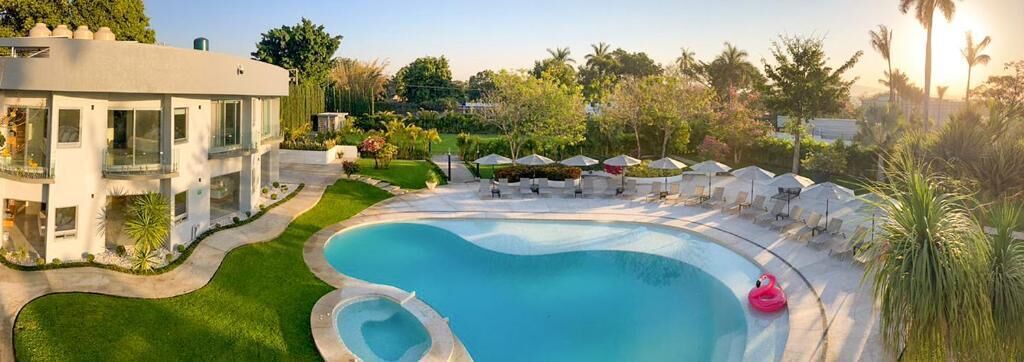 Una casa moderna con piscina, rodeada de césped cuidado y palmeras.