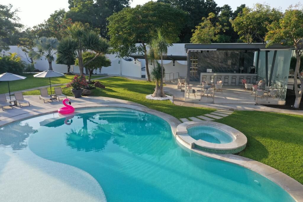 Una piscina con un flotador de flamenco rosa, rodeada por un césped cuidado y un área de estar al aire libre.