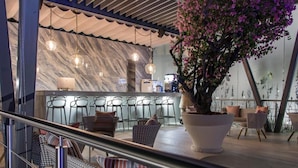 Un área de bar moderna con paredes de mármol, luces colgantes y una planta grande en maceta.