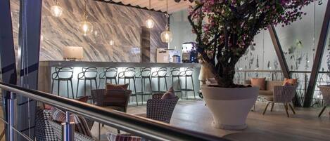A modern bar area with marble walls, hanging lights, and a large potted plant.