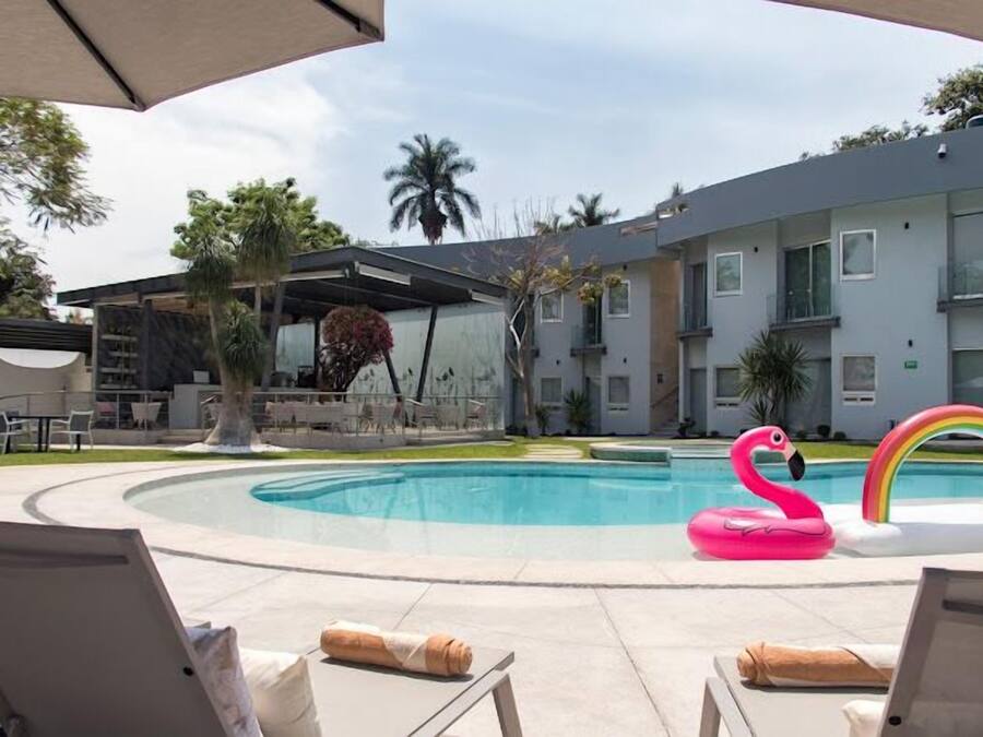 Un área de piscina con sillones de descanso, un flotador de flamenco y un flotador de arcoíris.