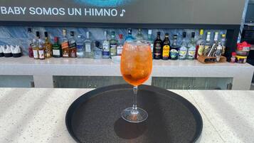 Uma área de bar com diversas garrafas de bebidas e um copo de drink vermelho sobre um apoio de bar preto.