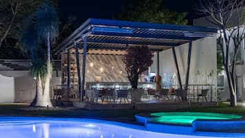 Un área junto a la piscina con una zona de estar techada, piscina y un edificio de diseño moderno.