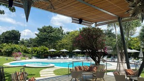 Zona junto a la piscina con sillones de descanso, una mesa y sombrillas.