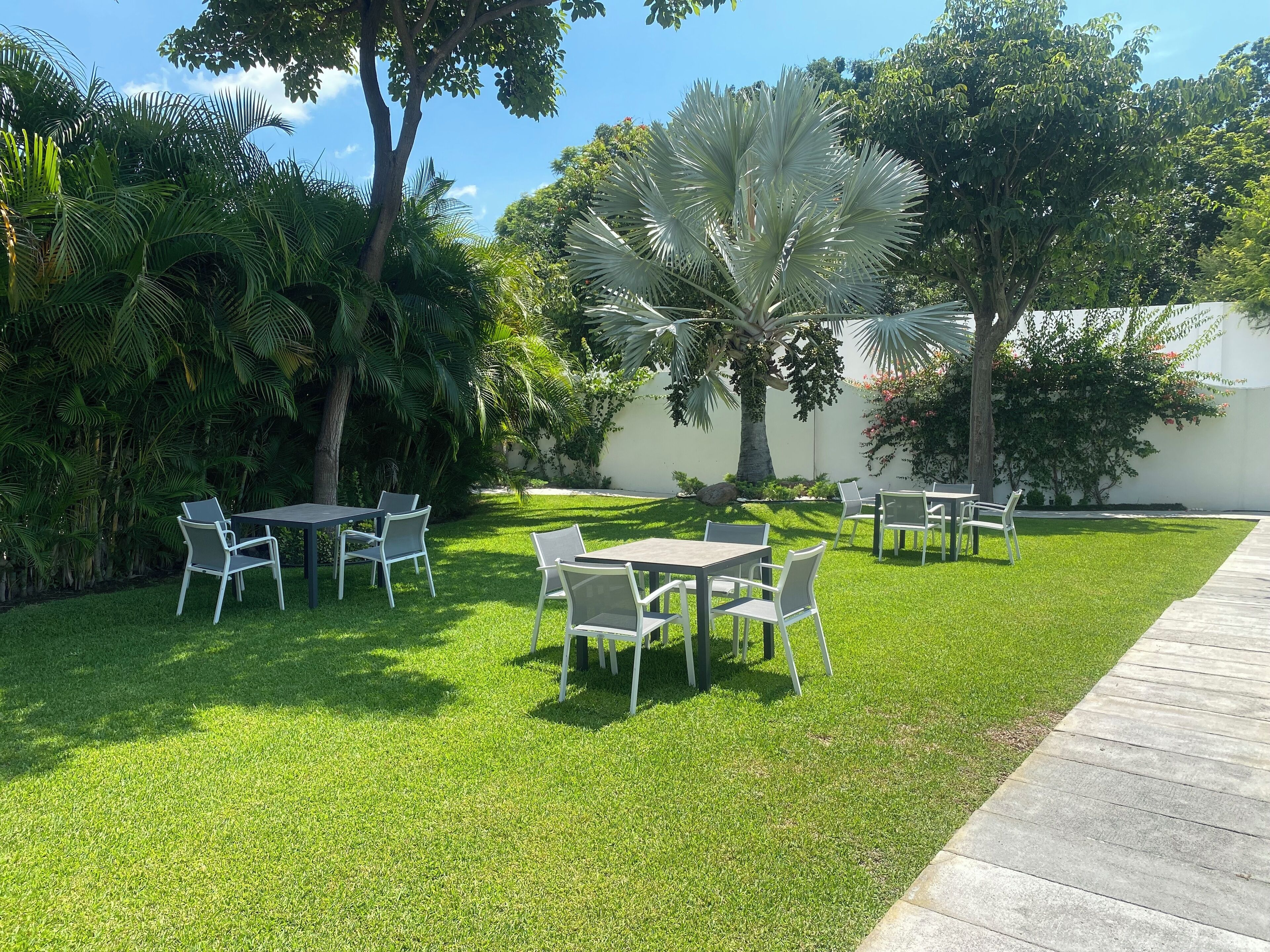 A well-maintained outdoor patio area with tables and chairs, surrounded by lush greenery and trees.