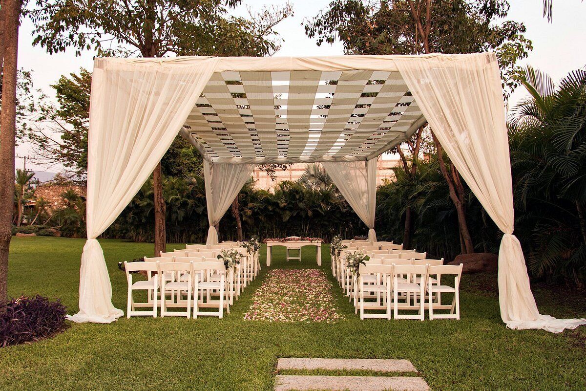 An outdoor wedding setup with a white canopy, white chairs, and a floral aisle.