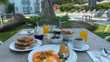 Una mesa de desayuno con tostadas, huevos revueltos, aguacate y un tazón de fruta.