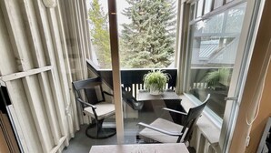 A modern balcony with a glass door, a wooden table, two chairs, and a potted plant.