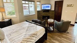 A modern bedroom with a large bed, a TV, a fireplace, and a view of the outdoors.