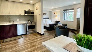 A modern kitchen with built-in appliances, a dining area with a table and chairs, and a bedroom with a bed and window.