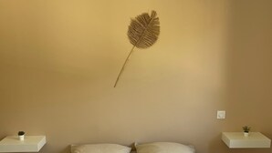 A neatly made bed with two pillows and rolled towels, a wall-mounted decorative item, and two bedside tables with small plants. - Gîte la Chotinière (Mareuil-sur-Cher)
