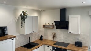 A modern kitchen with white cabinetry, a black countertop, a built-in oven, and a black range hood. - Gîte la Chotinière (Mareuil-sur-Cher)