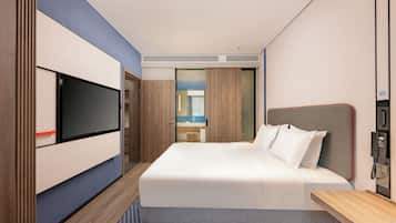 Una habitación de hotel moderna con una cama grande, un televisor de pantalla plana, un escritorio y un baño visible a través de una puerta abierta.