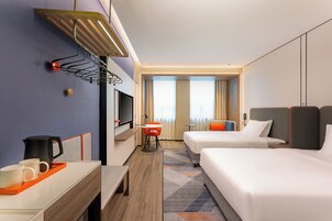 Habitación de hotel con dos camas, un escritorio con cafetera, televisión y vista al pasillo.