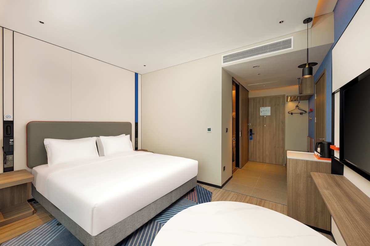 A modern hotel room with a large bed, a desk, a TV, and a bathroom visible through an open door.