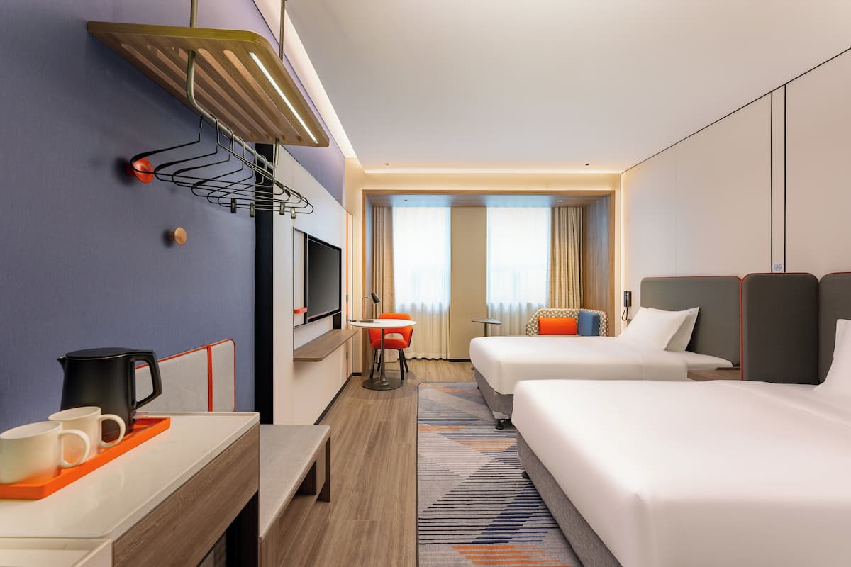 A hotel room with two beds, a desk with a coffee maker, a TV, and a window with curtains.