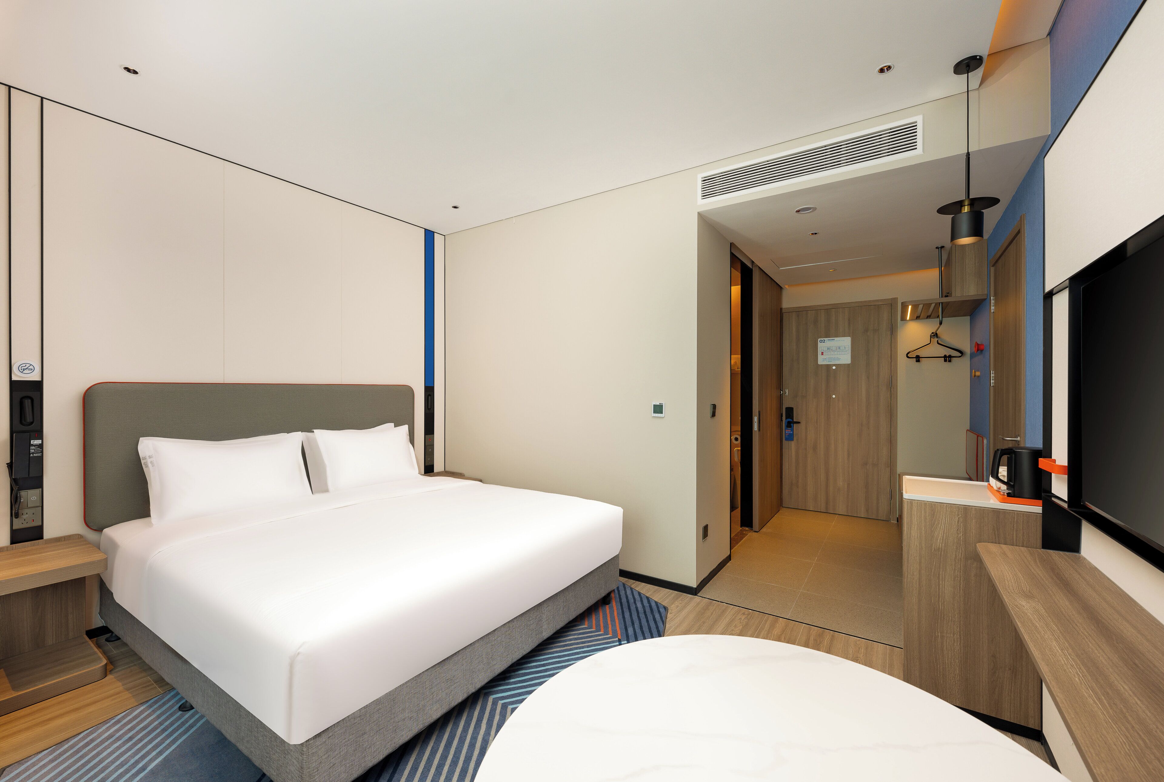 A modern hotel room with a large bed, a desk, a TV, and a bathroom visible through an open door.