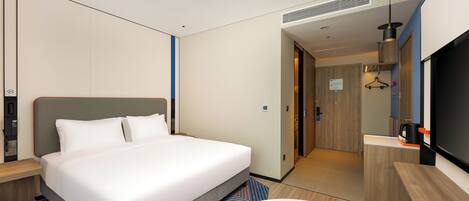 A modern hotel room with a large bed, a desk, a TV, and a bathroom visible through an open door.