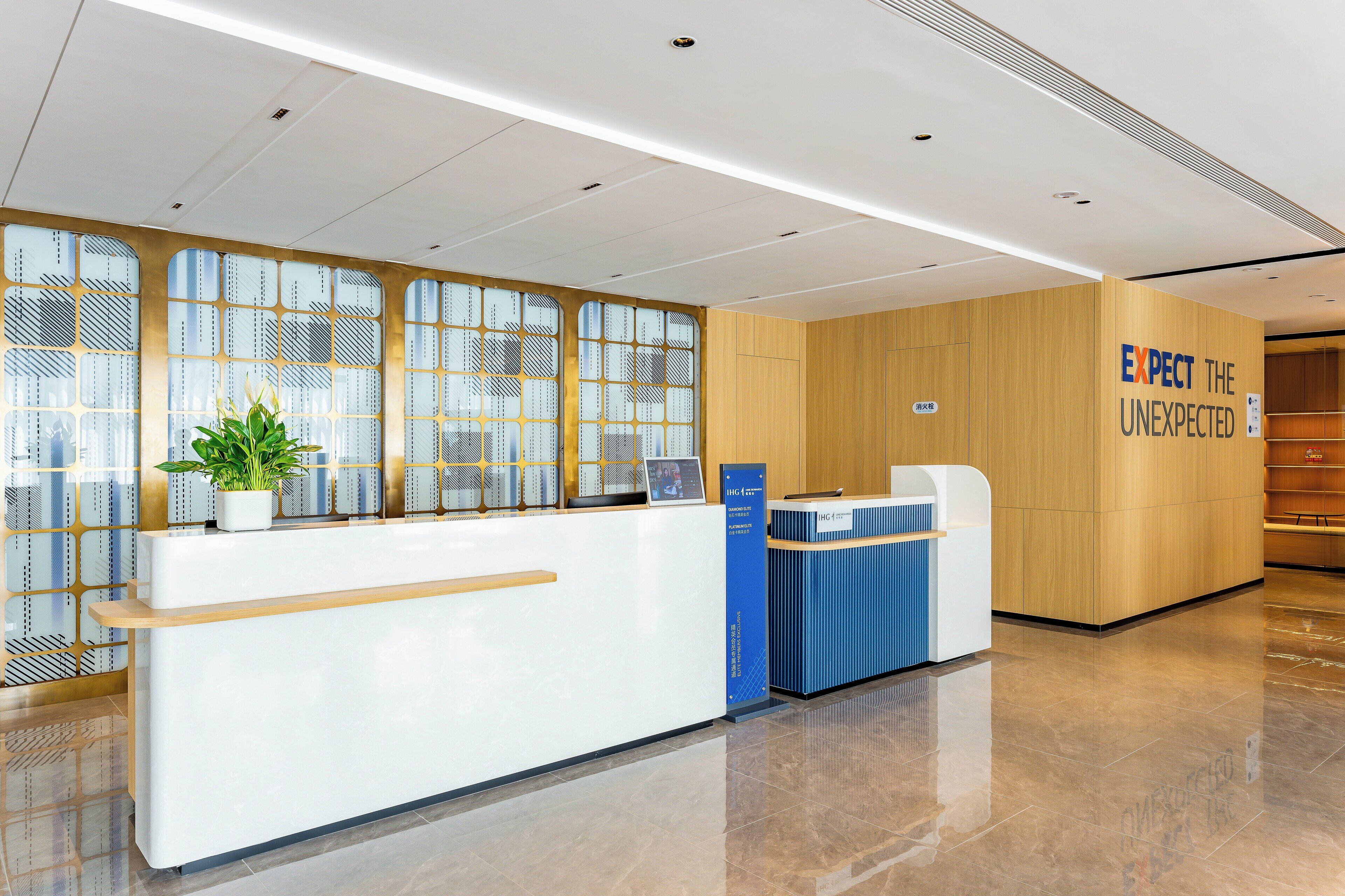 A reception area with a white reception desk, a blue counter, and a wooden wall with a sign that reads "EXPECT THE UNEXPECTED".