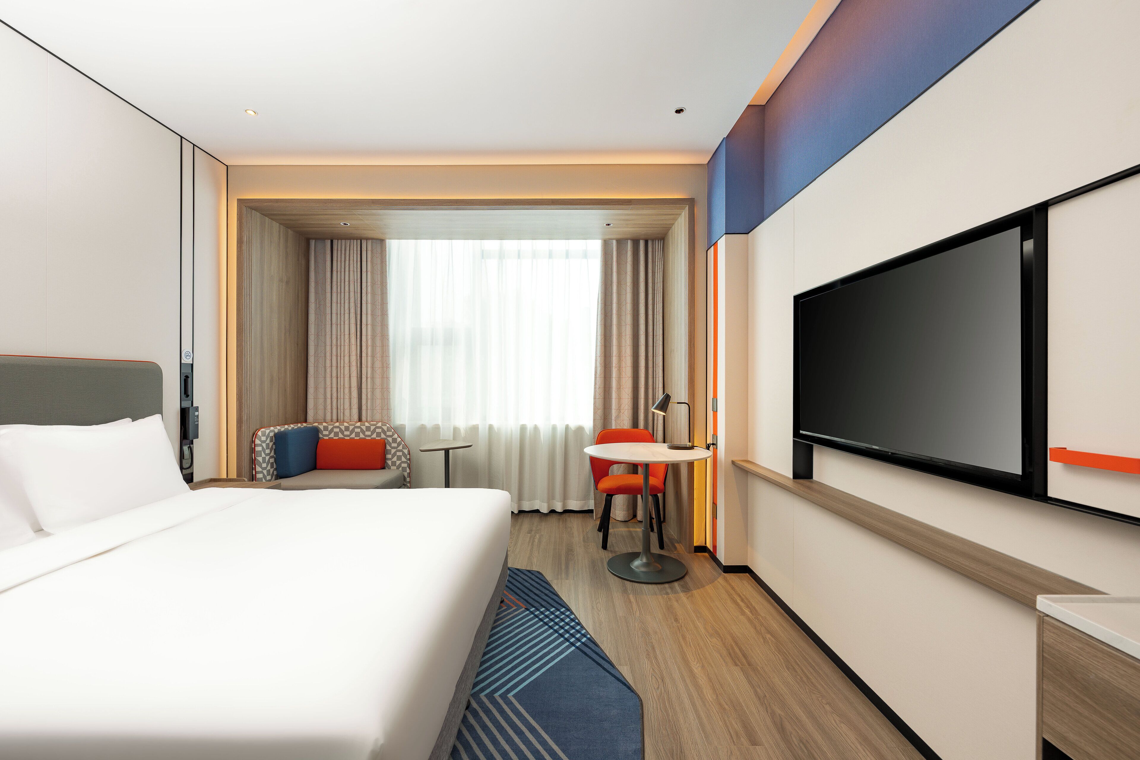A hotel room with a large bed, a TV, a desk, and a chair.