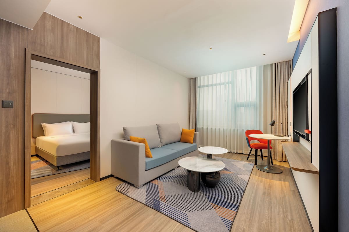 A modern hotel room with a sofa, a bed, a TV, and a small dining area.