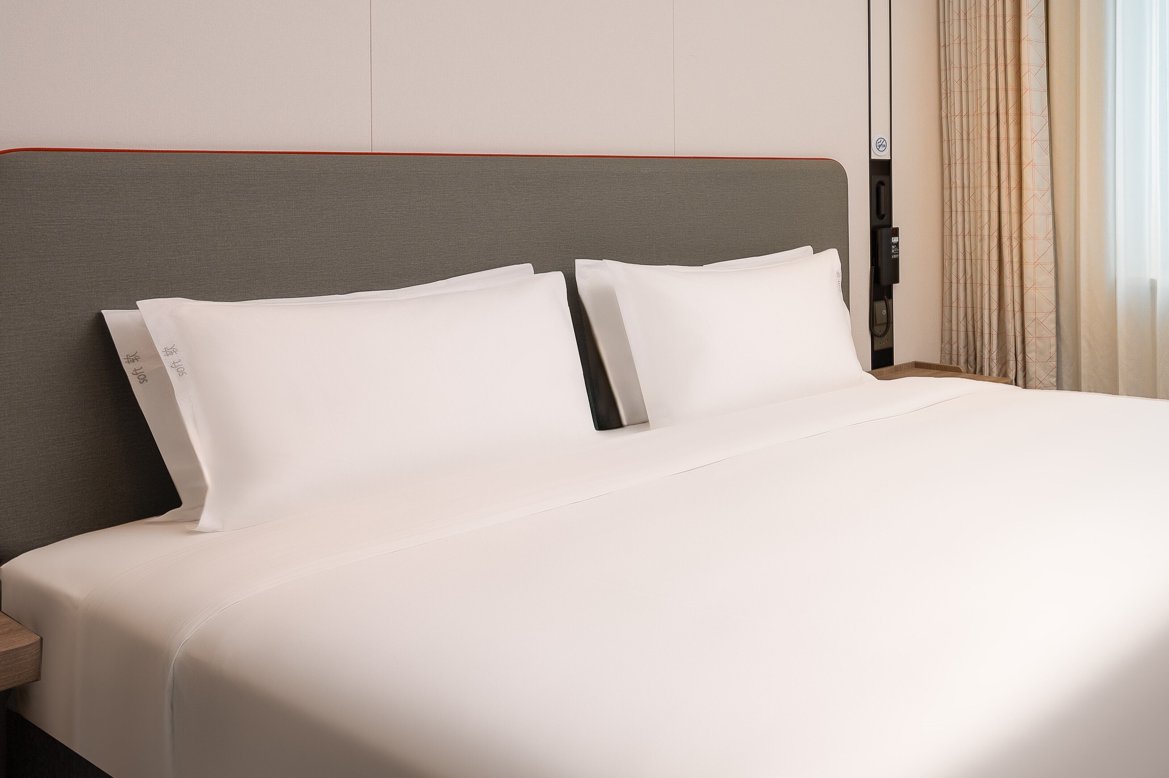A neatly made bed with white linens and a grey headboard.