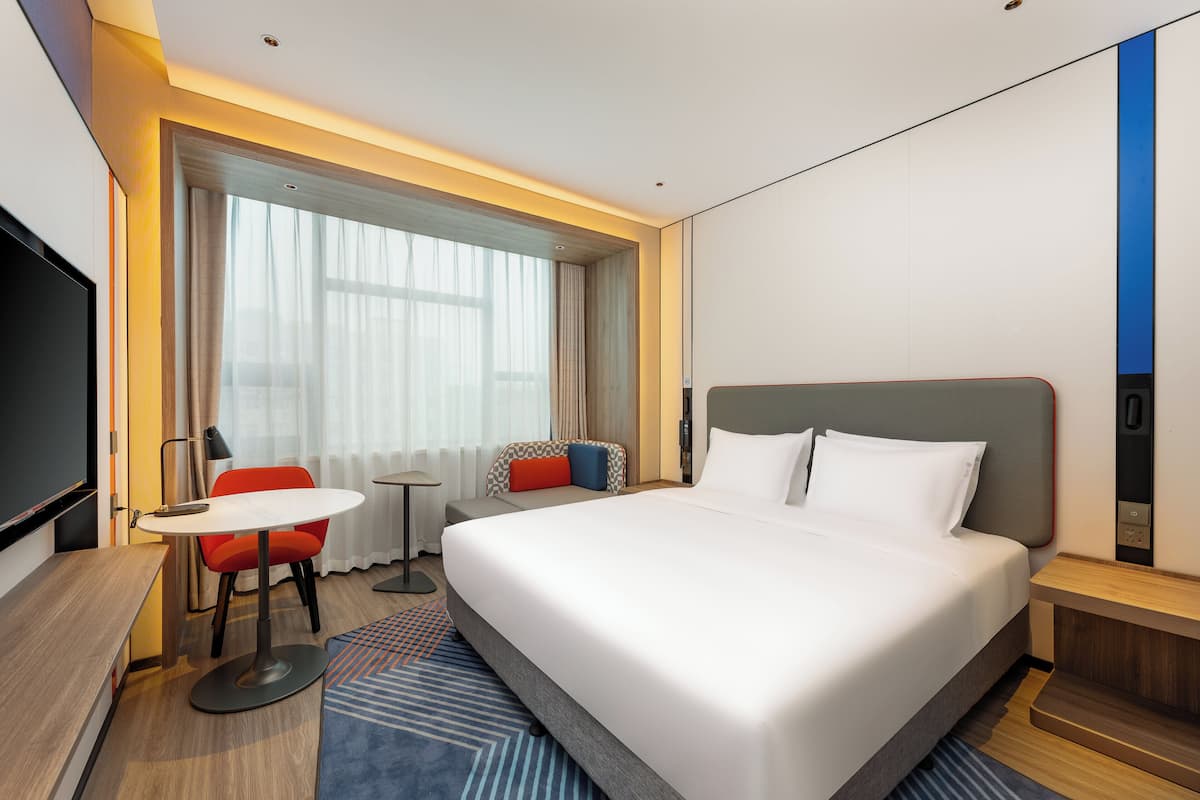 A hotel room with a large bed, a desk with a chair, a TV, and a window with curtains.