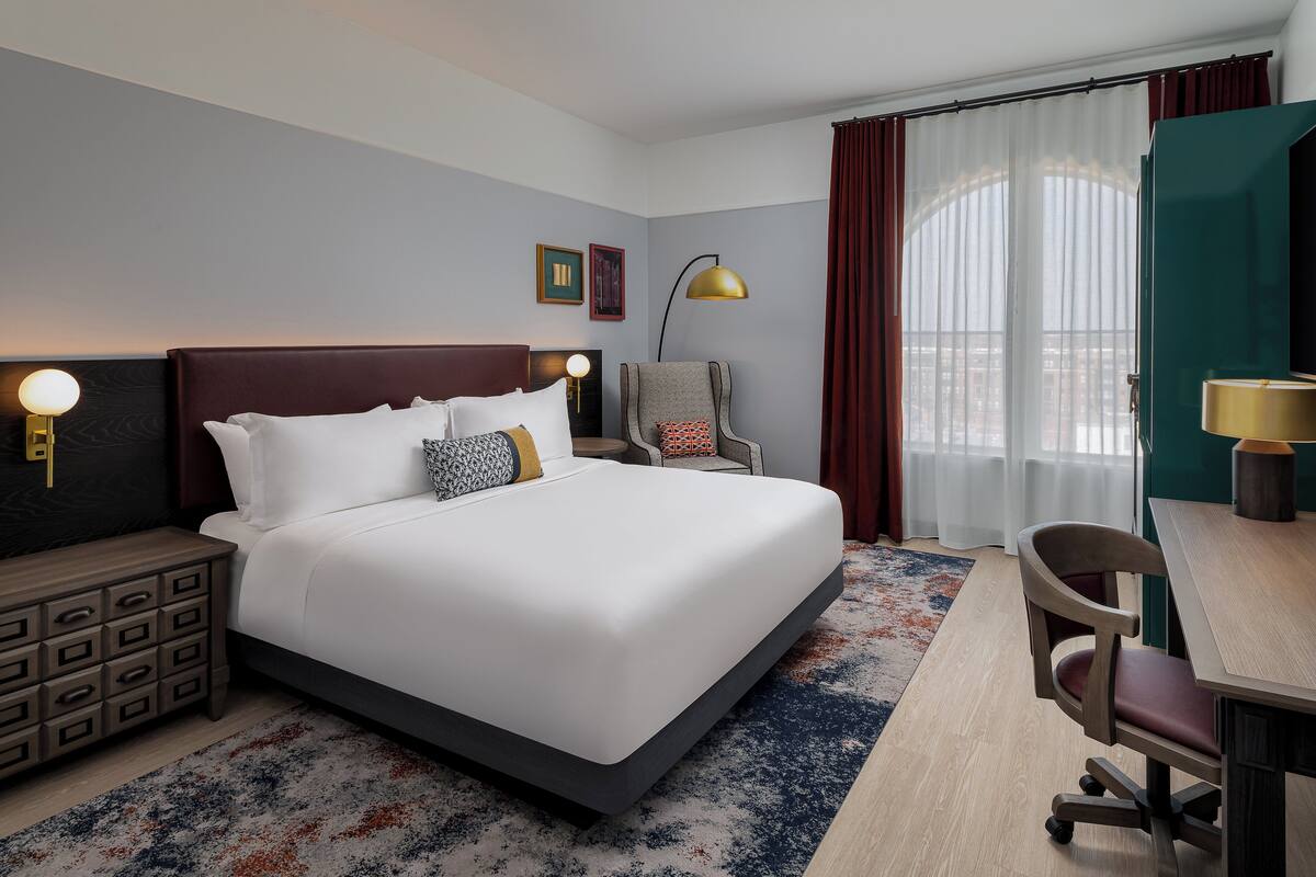 Una habitación de hotel con una cama grande, un escritorio, una silla, una mesita de noche y una lámpara.
