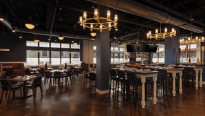 A spacious restaurant with high ceilings, exposed ductwork, and large windows. Tables and chairs are arranged for dining. - Hotel Indigo West Chester - Downtown by IHG (West Chester)