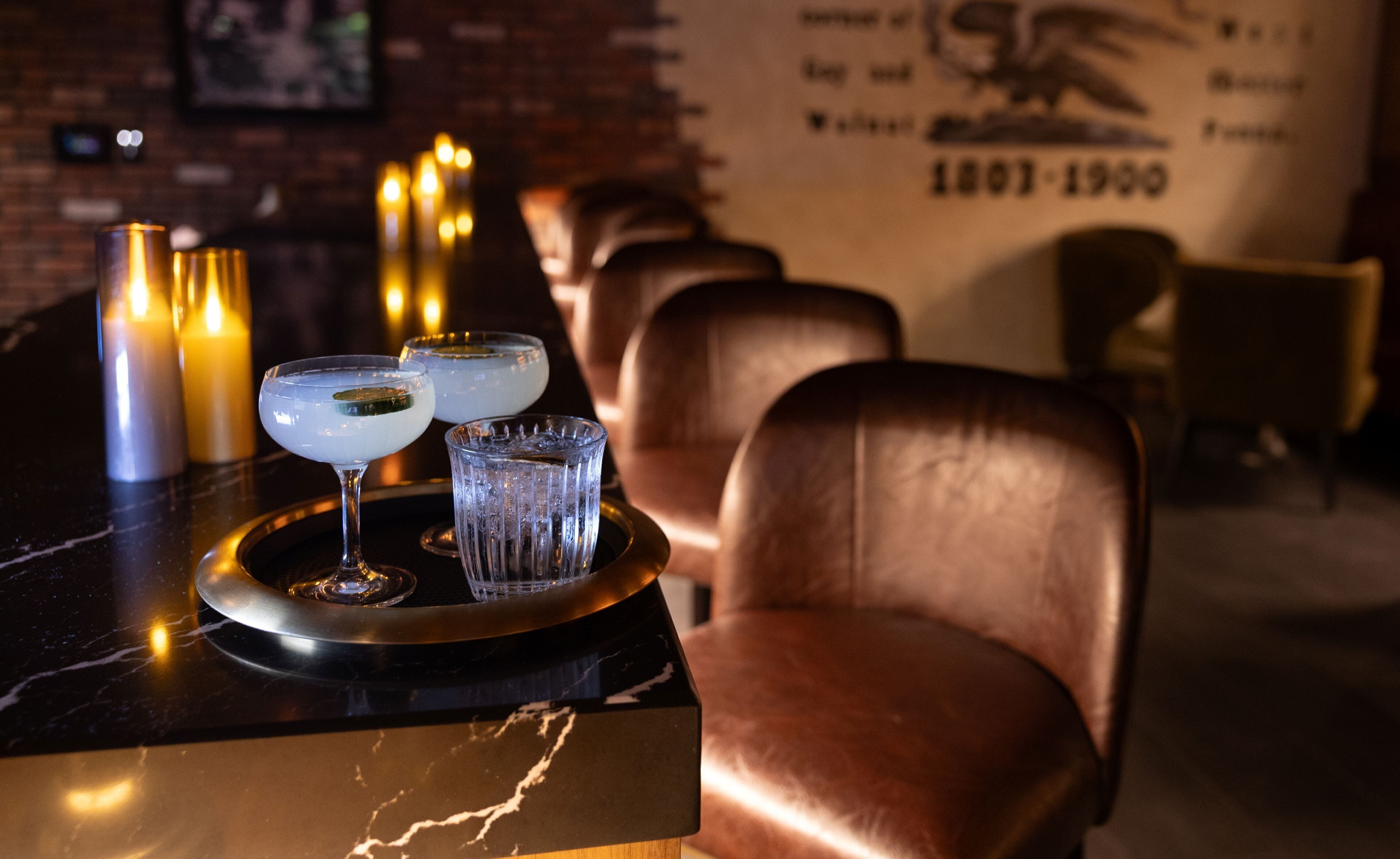 A bar area with a marble countertop, two glasses of a clear beverage, a tray, and candles.